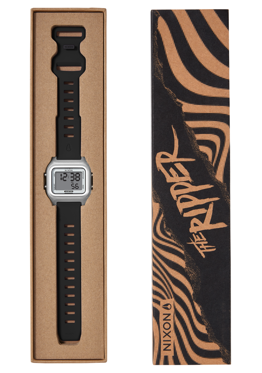 A silver digital watch with a black strap is displayed in a brown cardboard box next to its black and brown striped packaging that reads "THE RIPPER" and "NIXON". View 10